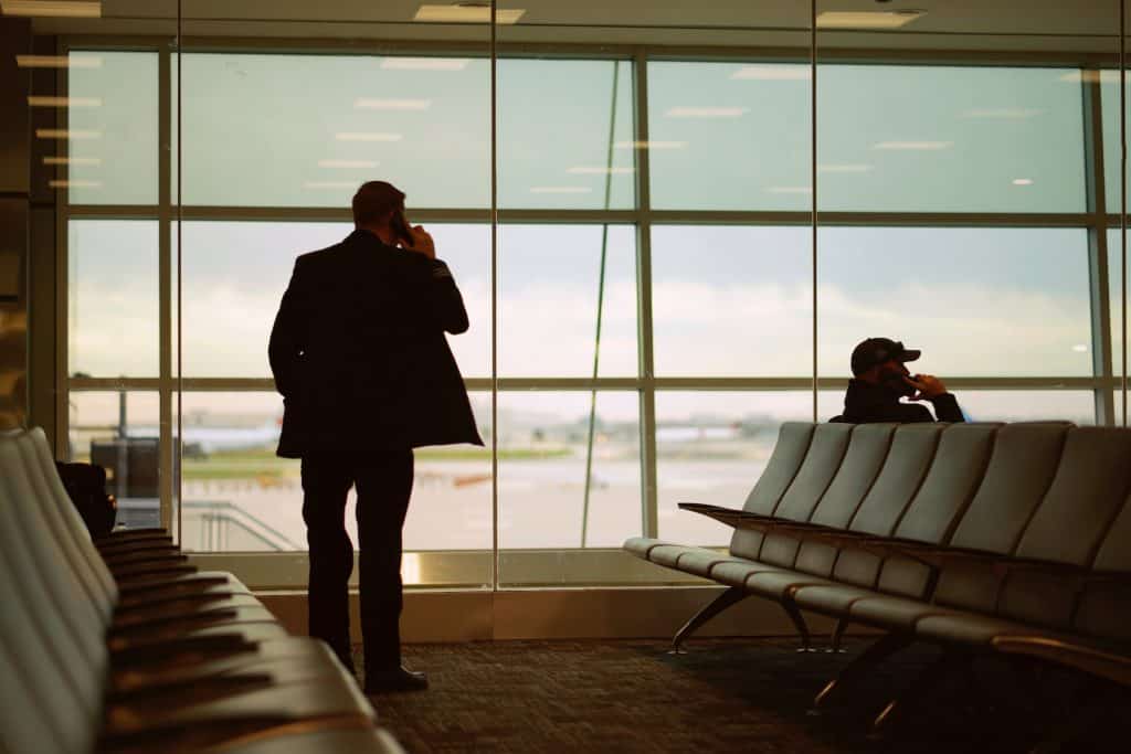 A man in an airport, talking on his cell phone, stares outside the window at the tarmac.