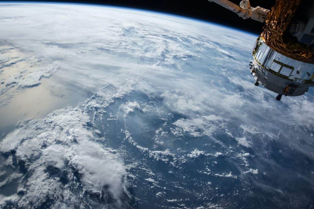 A photo of the earth from space, featuring a small part of a spaceship in the foreground.