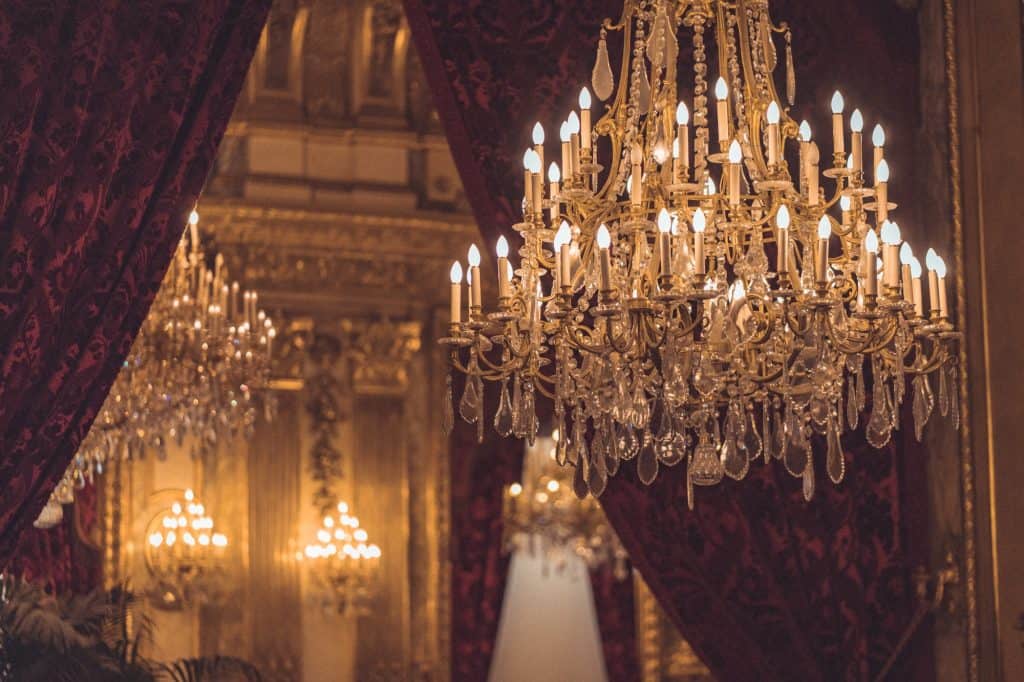 A chandelier in front of a mirrored wall. Red curtains are open but still visible in front of the mirror.
