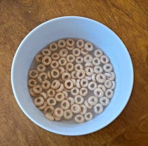 A picture of a white bowl with water and Cheerios cereal.